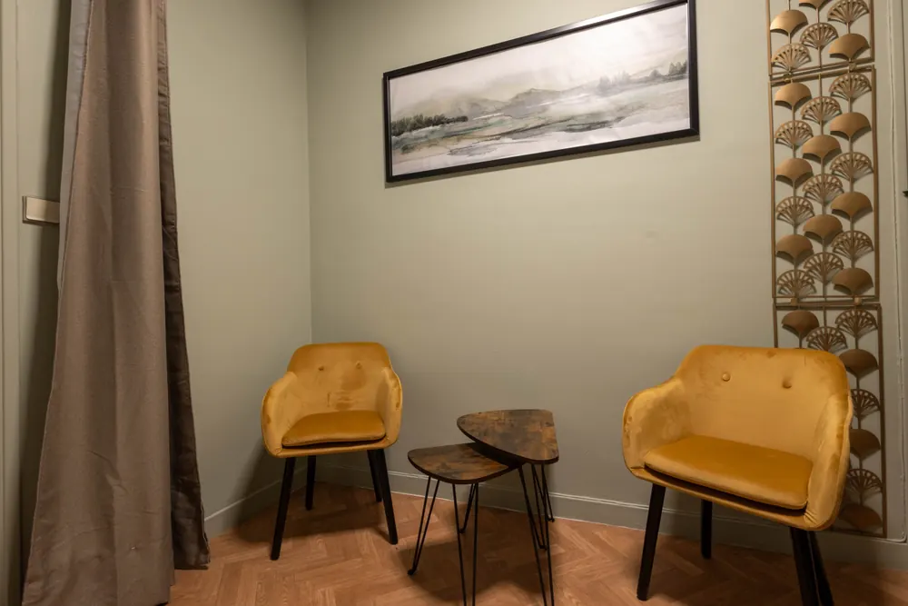Coin entretien du cabinet de kinésiologie à Bayonne : deux fauteuils moutarde face à face, une table d'appoint et une aquarelle de paysage