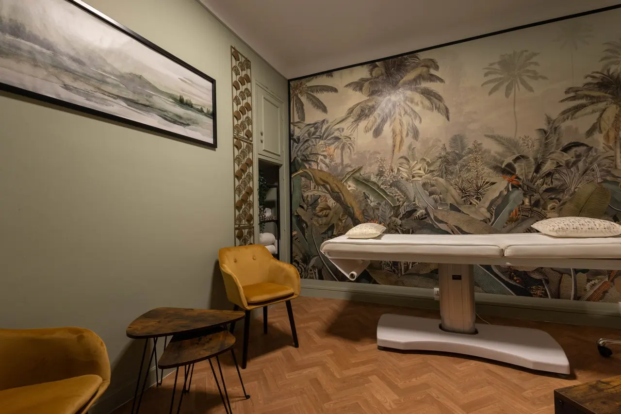 Cabinet de reiki et de kinésiologie à Bayonne : table de soin devant une fresque de palmiers, murs vert sauge et fauteuils moutarde